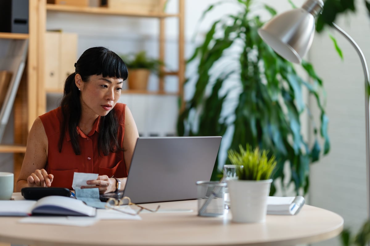 Mujer emprendedora revisando las cuentas de su negocio en la computadora, con calculadora y recibos sobre el escritorio