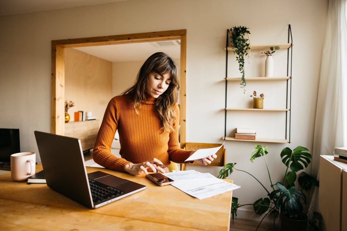 Emprendedora revisando las cuentas de su pequeño negocio con laptop y teléfono